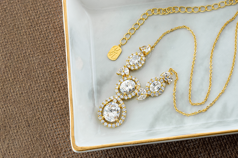 Gold necklace with large round and teardrop clear gemstones on a white and gold-edged tray.