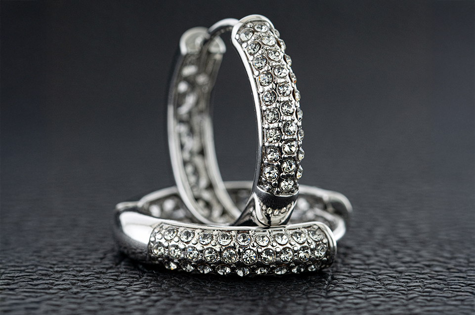 Pair of silver hoop earrings encrusted with multiple rows of clear rhinestones on a textured black surface.