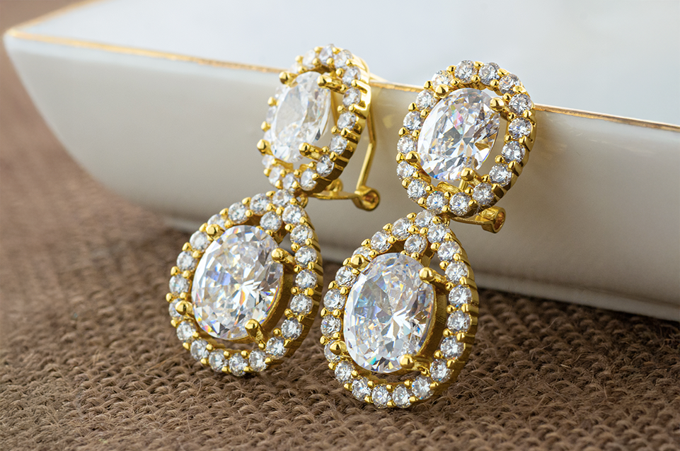 Pair of gold drop earrings with large oval-cut clear gemstones surrounded by smaller round clear stones.