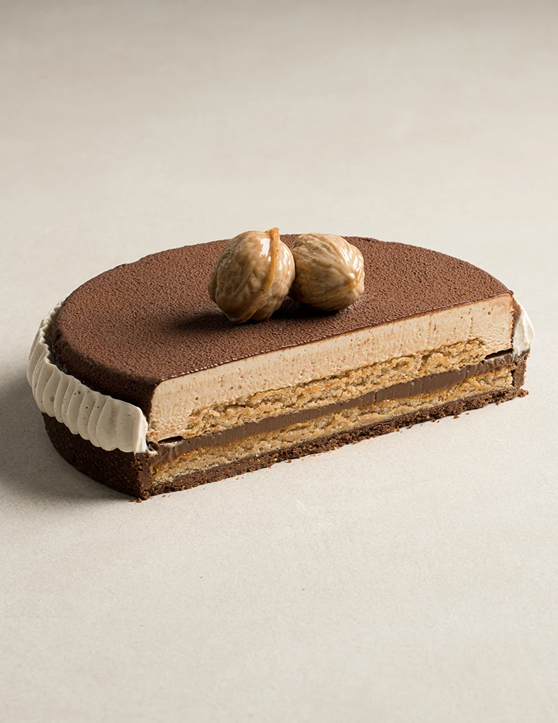 Nut Noir cake cut in half showing chocolate almond tart, pecan biscuit, nut praline, chocolate crémeux, and nut mousse layers.