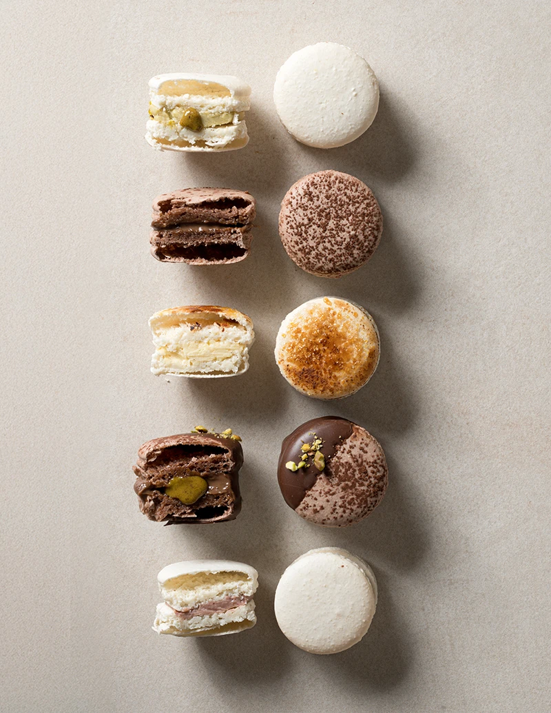 Assorted macarons cut in half showing pistachio, chocolate, crème brûlée, mixed berry, and Dubai chocolate fillings.