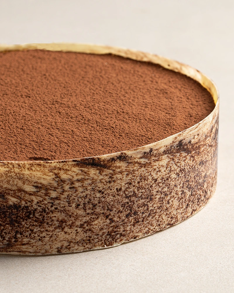 Classic Tiramisu with cocoa powder finish, white chocolate décor, and layered vanilla cream.