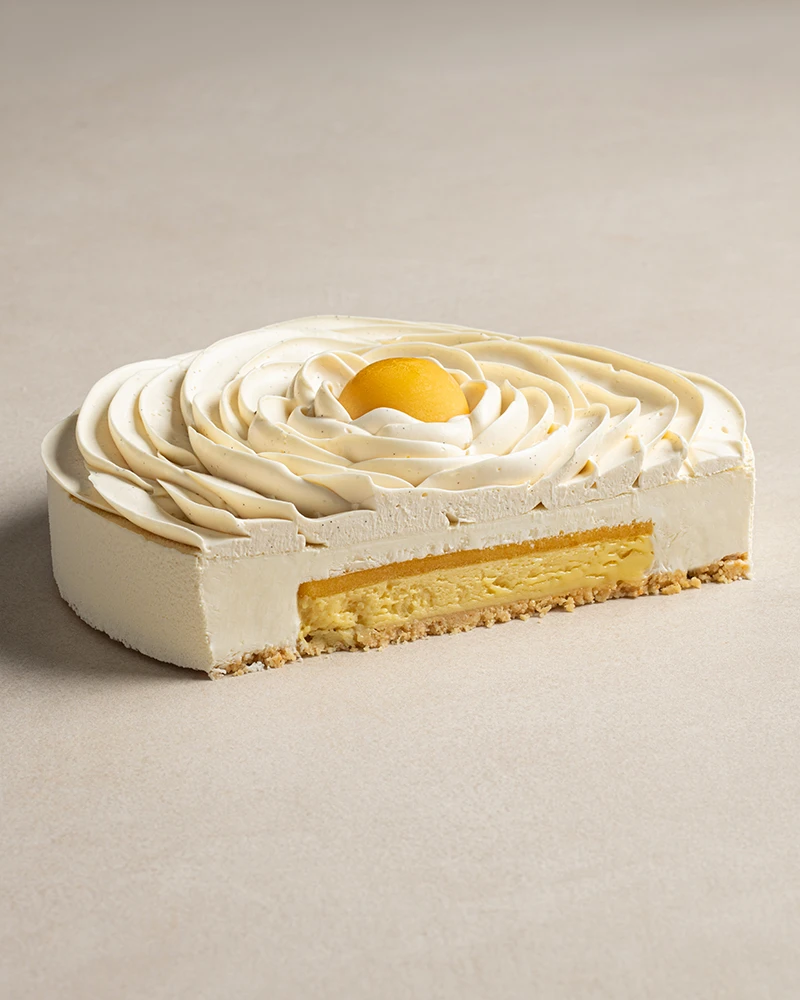 Exotic Cheesecake cut in half showing crunch base, passion fruit crémeux, mango jam, and cheesecake mousse layers.