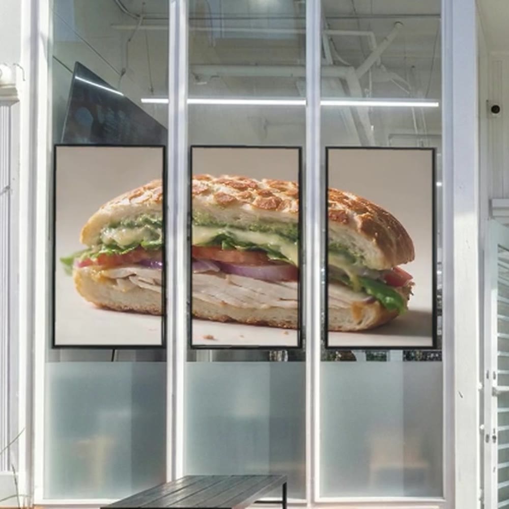 Storefront window with three screens showing a sandwich (concept).