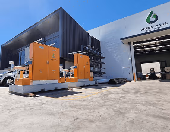 Industrial equipment units outside a modern building with a Greenlands Equipment logo on a clear, sunny day.