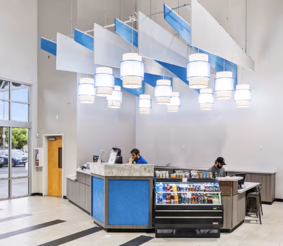Modern reception area with blue and gray counters, hanging white cylindrical lights, and a display case with snacks and drinks.