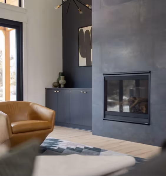 Modern living room with a built-in fireplace, a tan leather armchair, dark cabinetry, and large window letting in natural light.