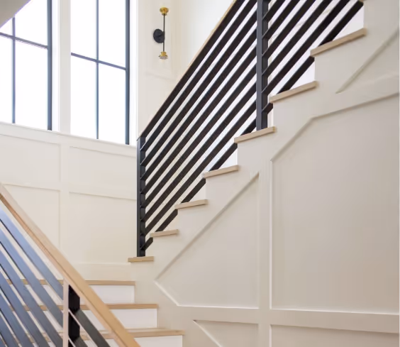 Modern indoor staircase with black horizontal metal railings, light wood steps, and large windows.