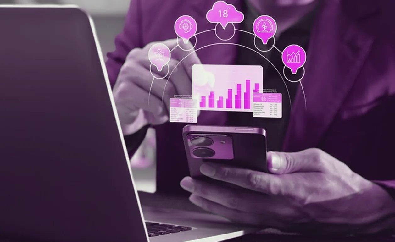 Person holding a smartphone and interacting with floating digital data charts and icons above a laptop.