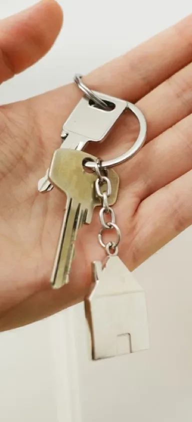 Hand holding a keyring with two metal keys and a house-shaped keychain.