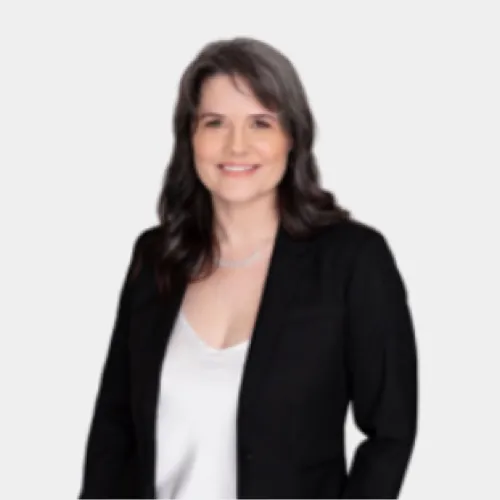 Smiling woman with shoulder-length dark hair wearing a black blazer over a white top against a light background.