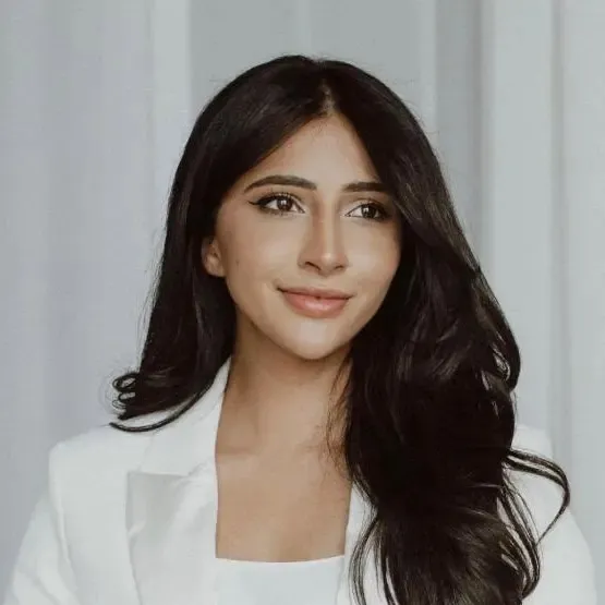 Portrait of a woman with long dark hair wearing a white blazer, smiling slightly and looking to the side.