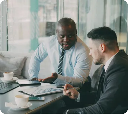 Two business professionals discussing documents and data charts over coffee at a table.