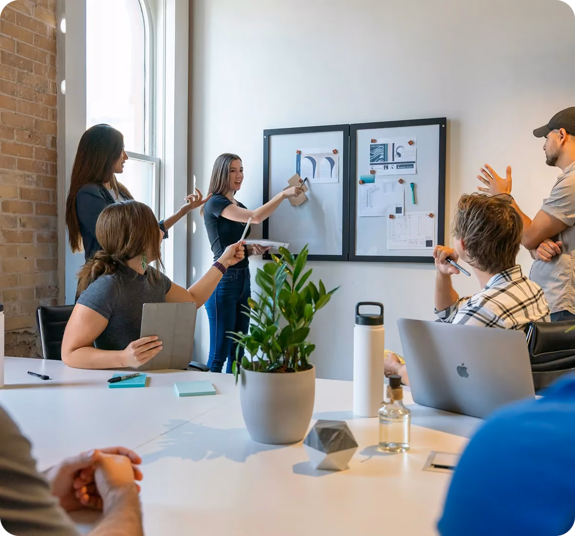 A group of coworkers discussing ideas in a meeting room with notes on a whiteboard.