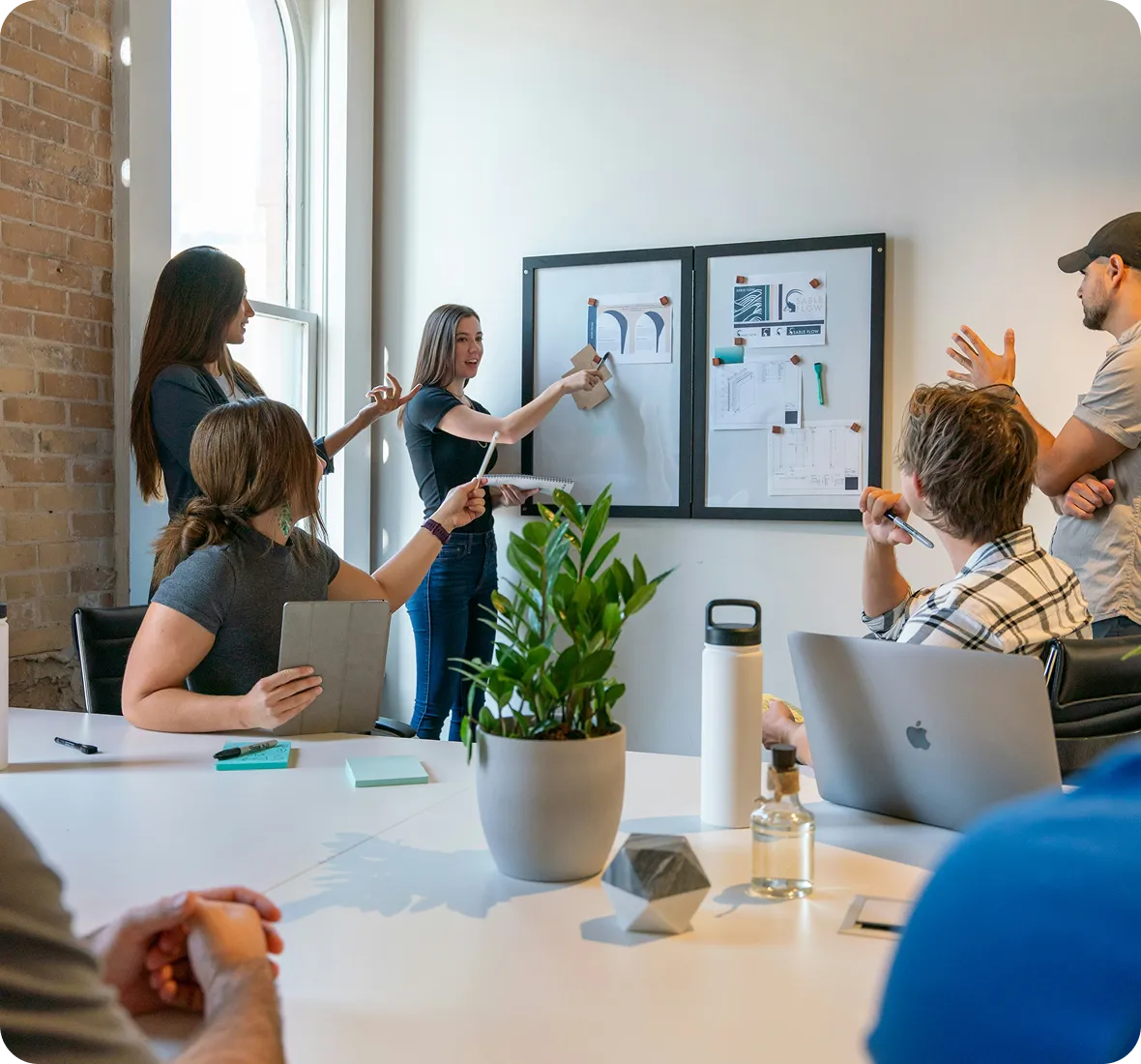 A group of coworkers discussing ideas in a meeting room with notes on a whiteboard.