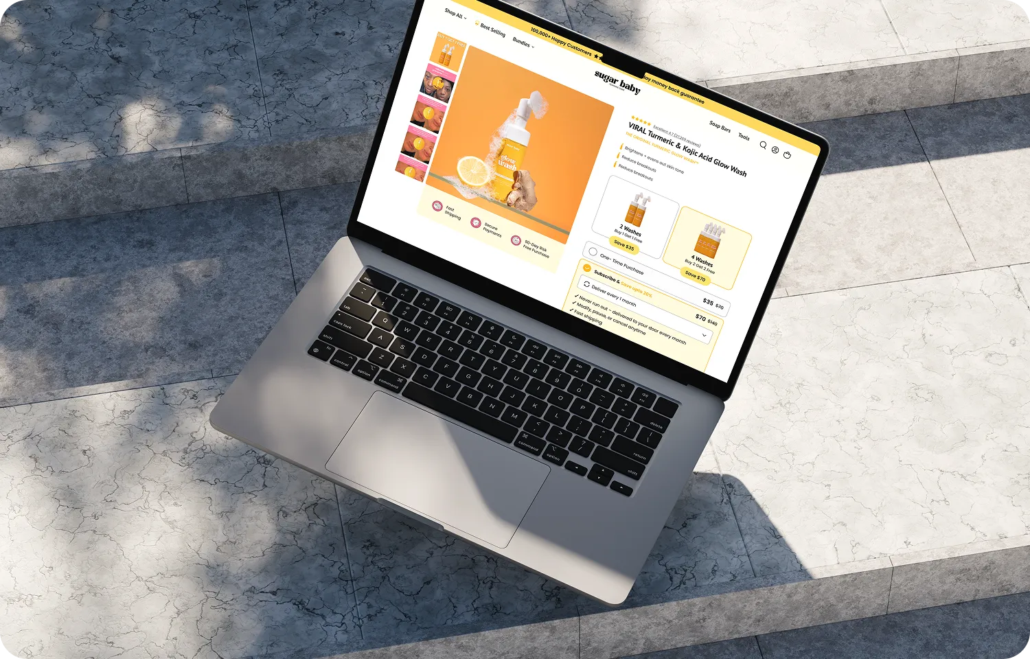 Laptop on stone steps showing an online store page for Turmeric & Kojic Acid Glow Wash skincare product.