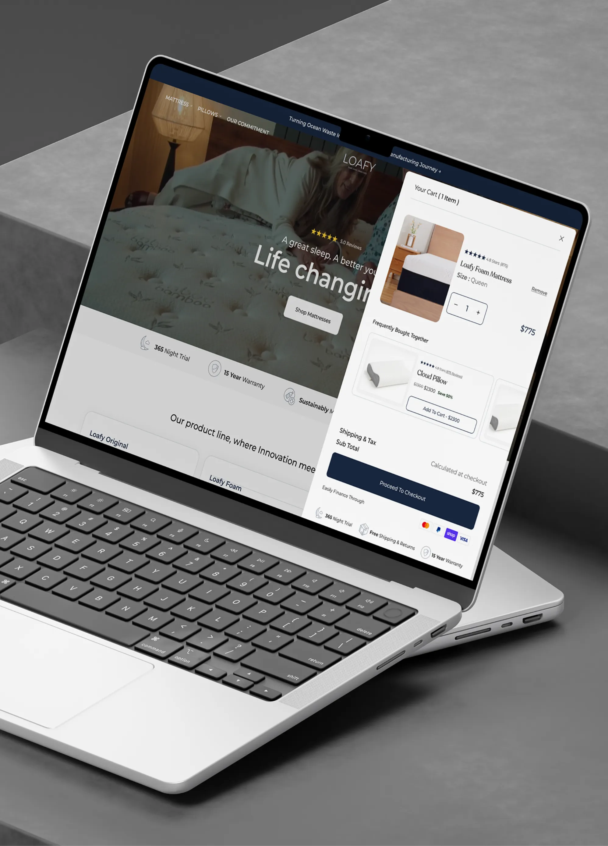 Laptop on gray surface displaying Loafy mattress website with cart showing queen mattress priced at $775.