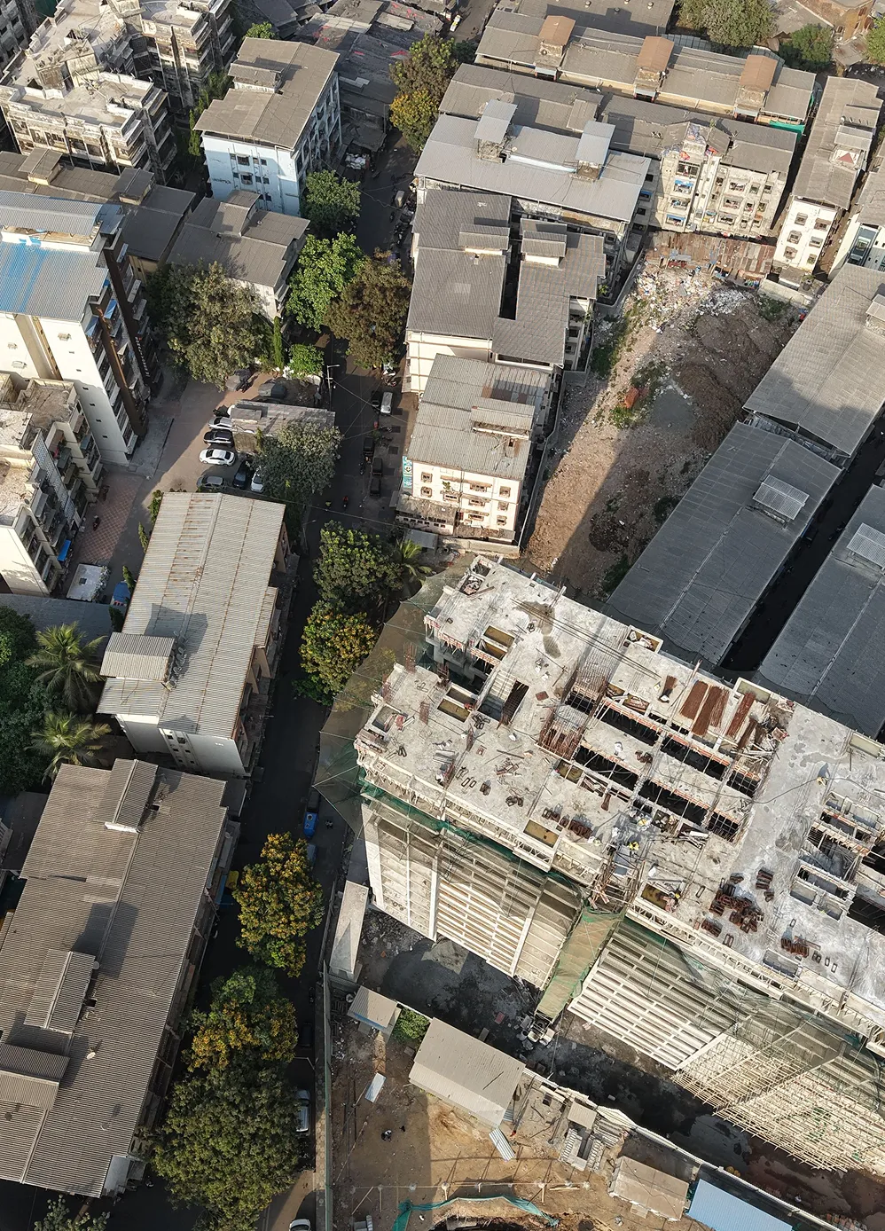 Aerial view of urban buildings with one under construction and surrounding trees and roads.