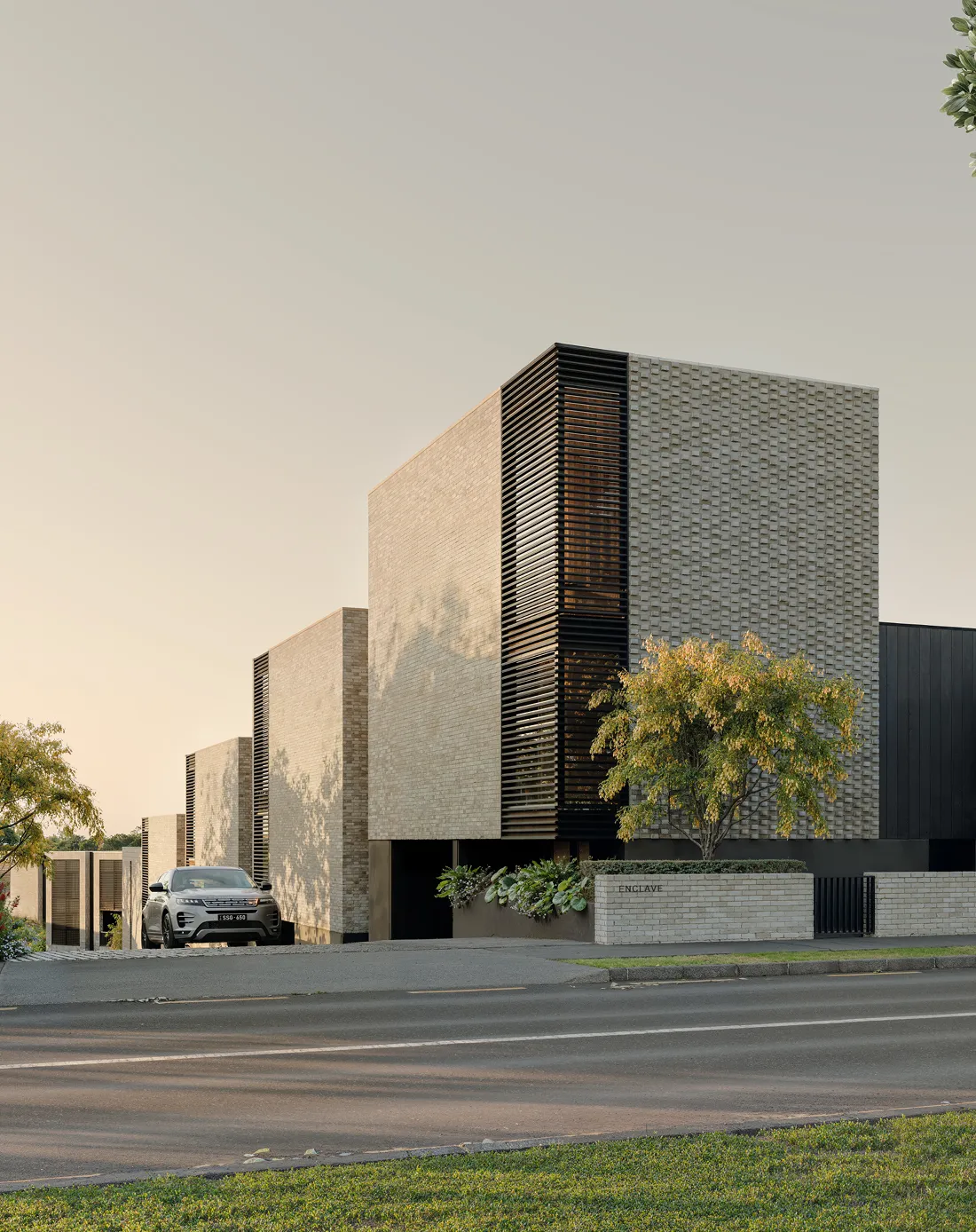 Modern beige brick building with black accents, greenery, and a parked silver car outside.