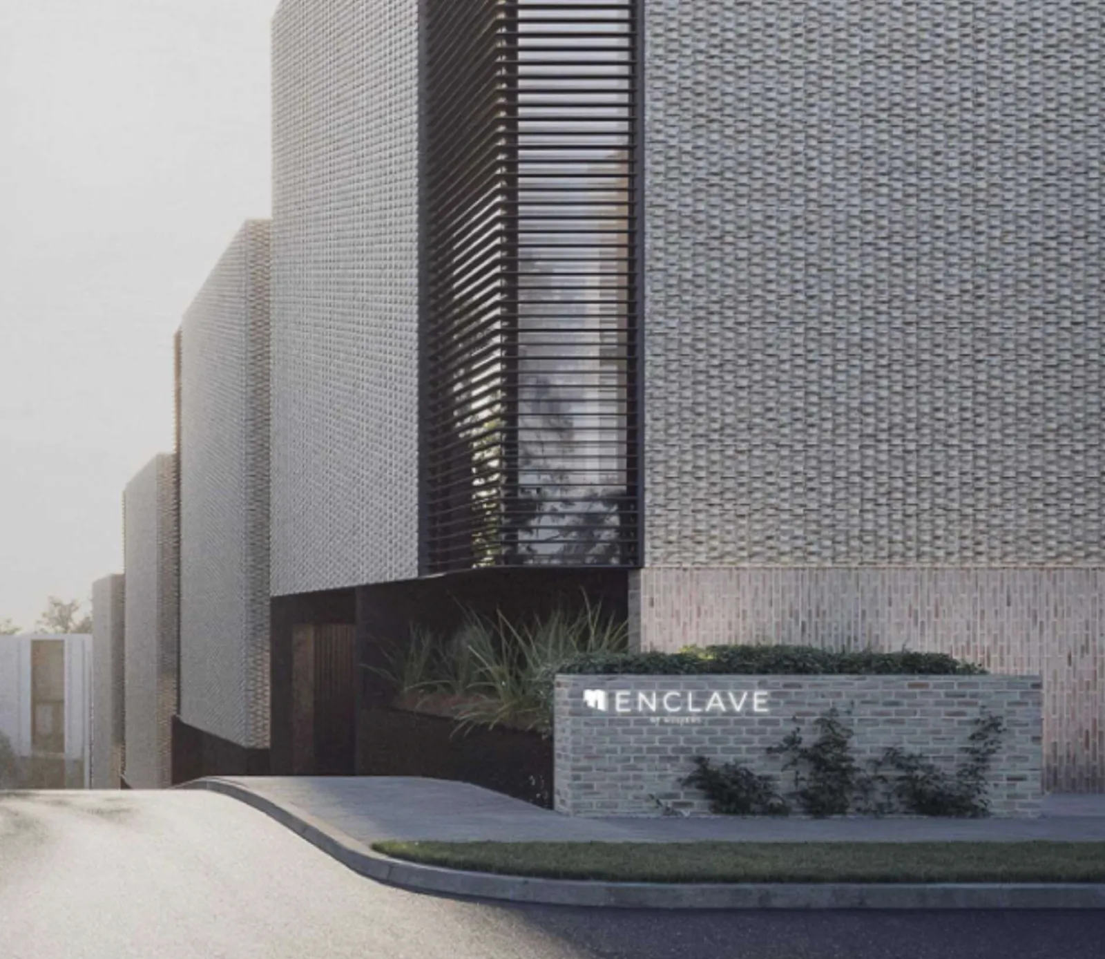 Modern building exterior with textured walls and a sign reading 'ENCLAVE' near greenery.