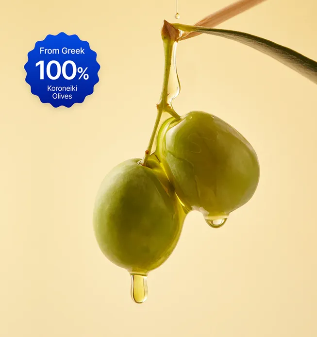 Two green Koroneiki olives on a branch with oil dripping against a light background.