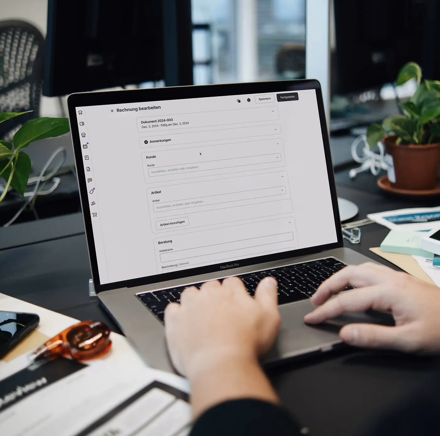 Person using laptop with invoice editing software in German, plants and office items on desk.