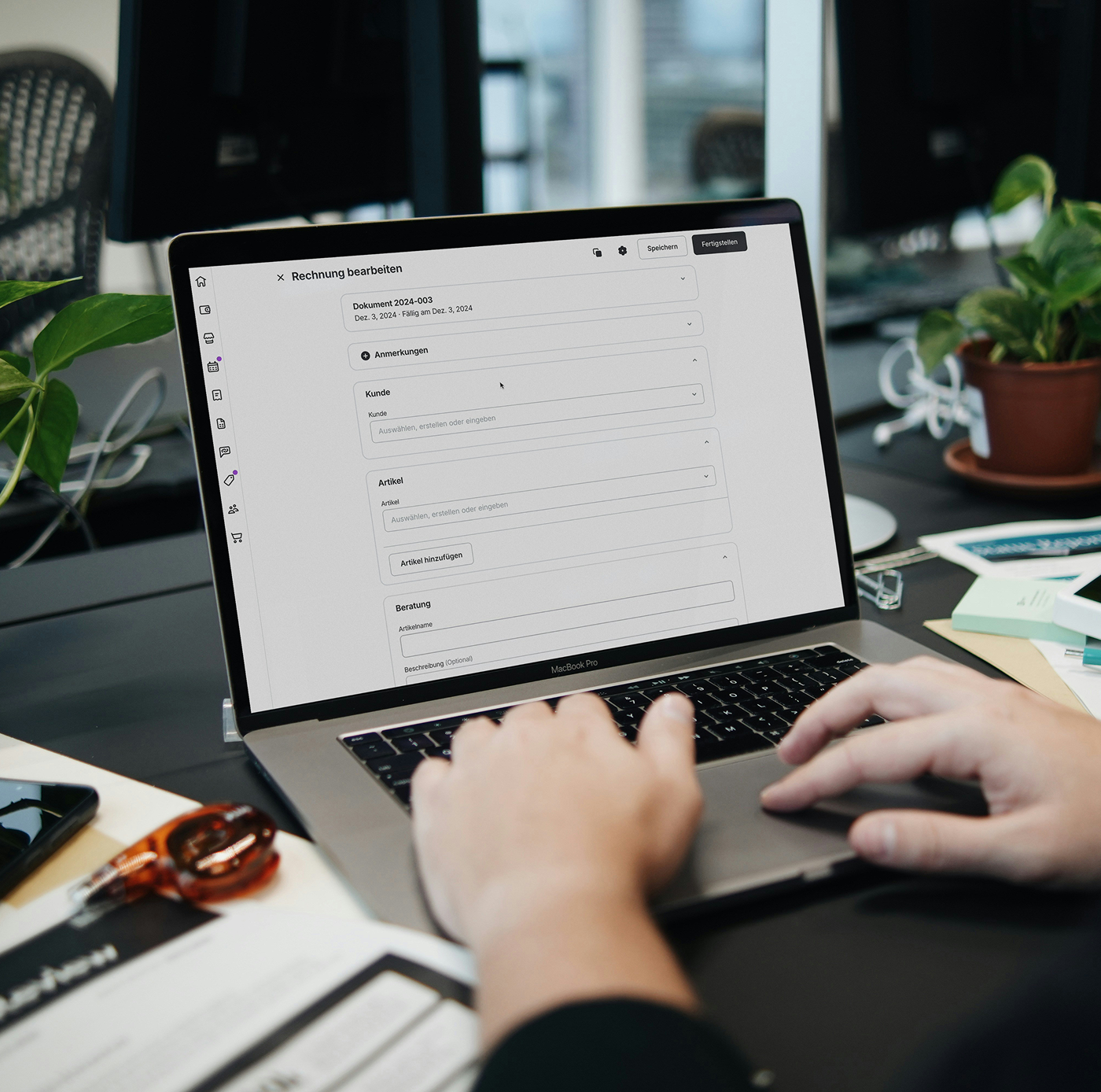 Person using laptop with invoice editing software in German, plants and office items on desk.