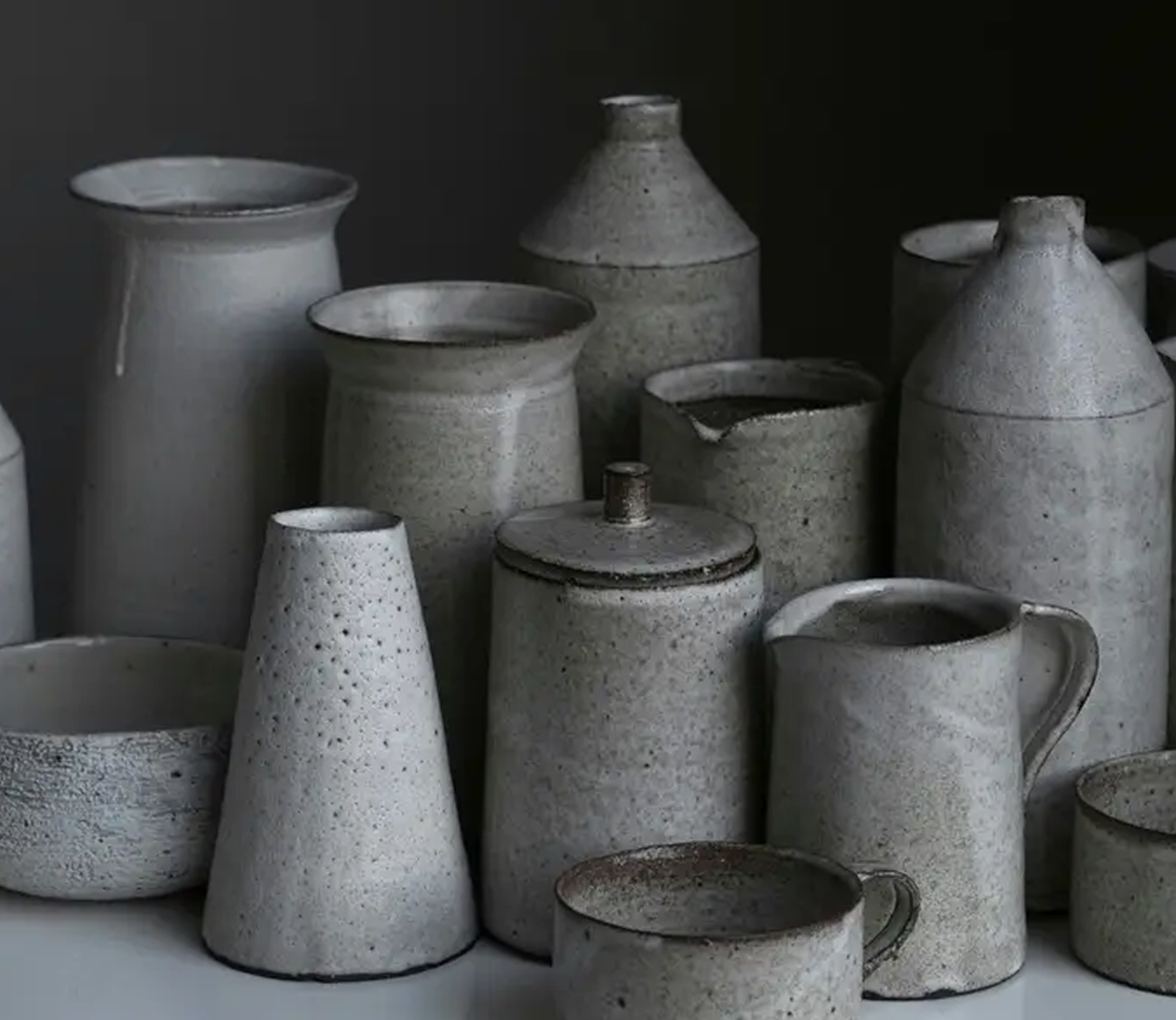 Collection of rustic gray ceramic pottery including vases, jars, pitchers, and cups on a surface.
