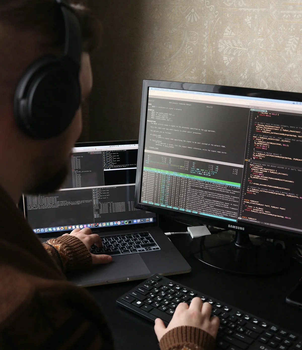 Person wearing headphones working on coding and terminal commands on a laptop and external monitor.