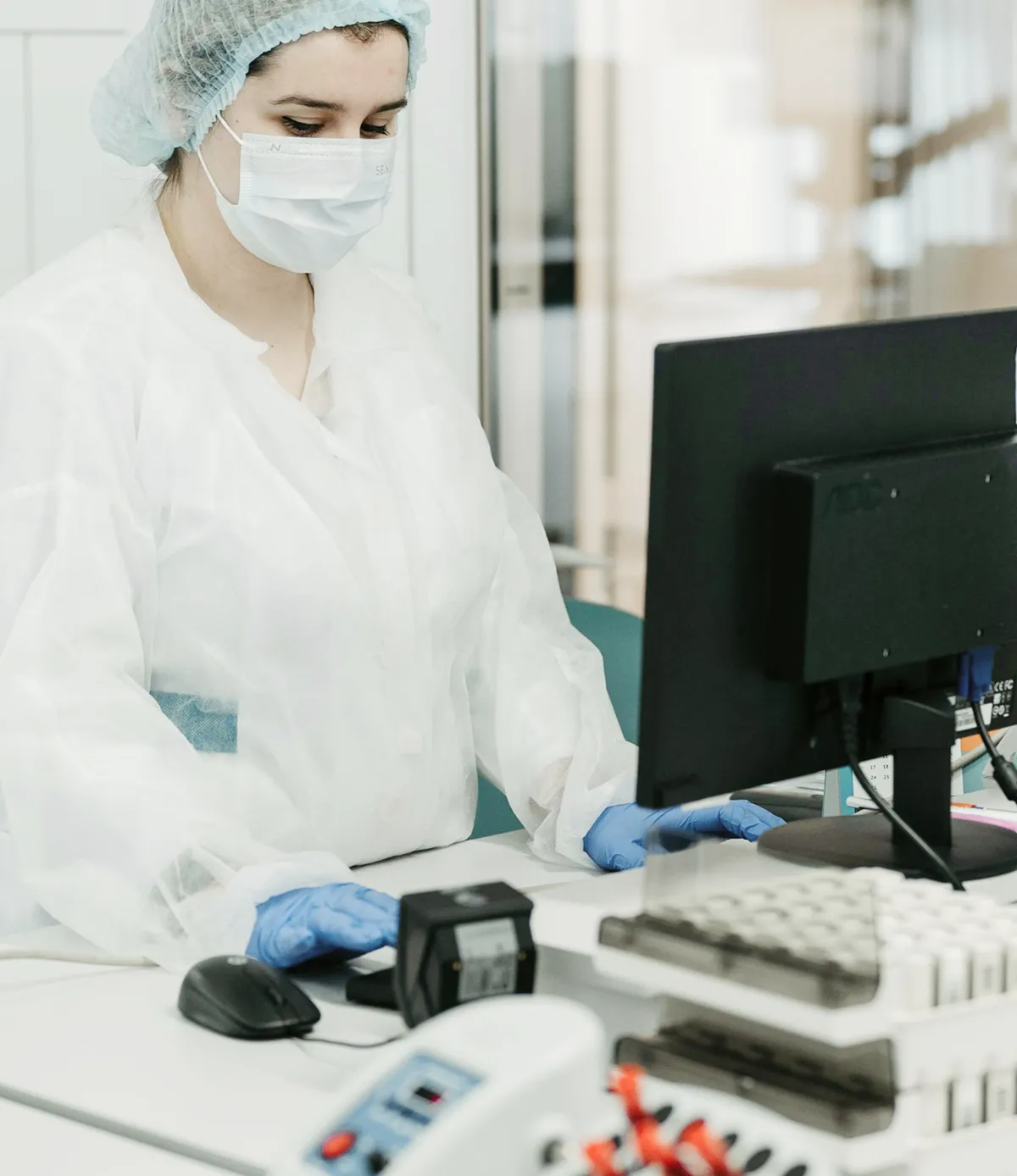 Lab worker in protective gear using a computer in a clinical laboratory setting.