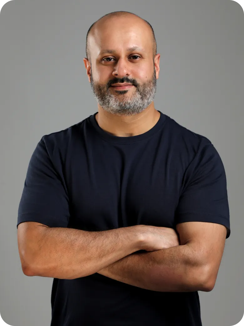 Man with a beard and mustache wearing a black t-shirt, arms crossed, against a gray background.