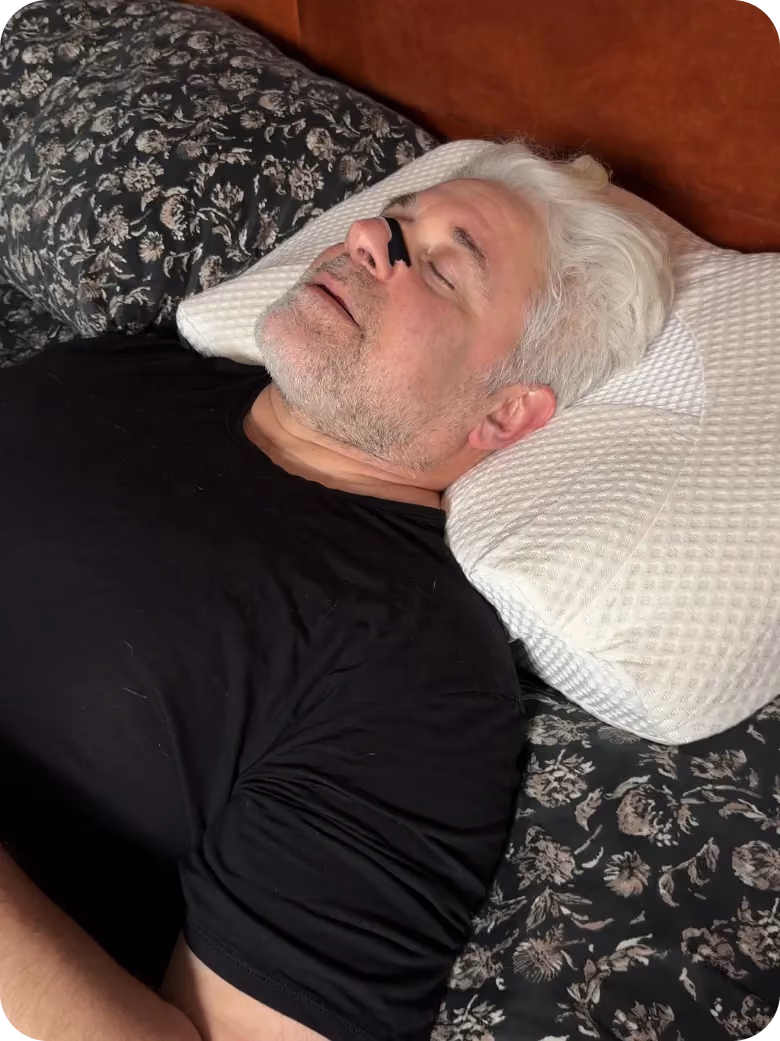 Older man sleeping on patterned pillow with a black nose strip on his nose.