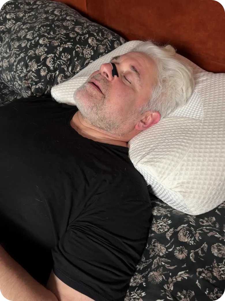 Older man sleeping on patterned pillow with a black nose strip on his nose.