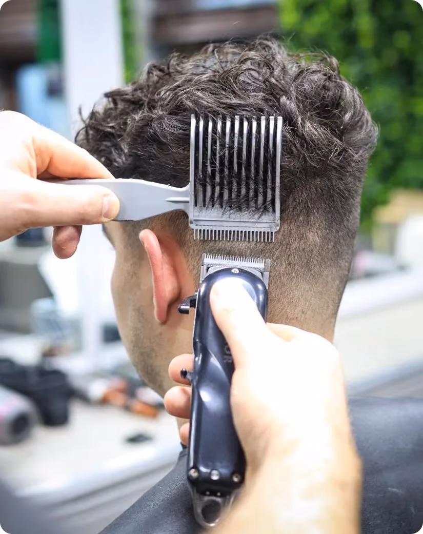 Close-up of man getting a fade haircut with clippers and comb at a barbershop.