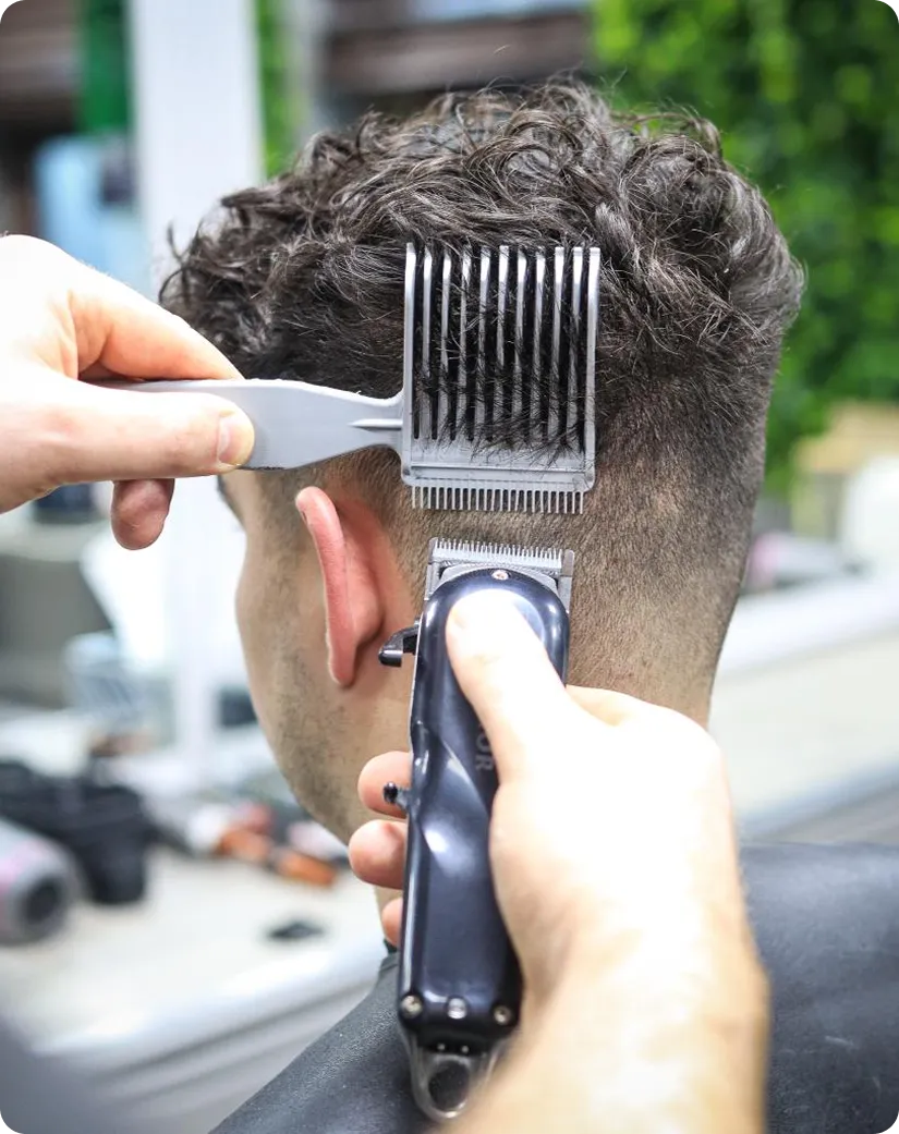 Close-up of man getting a fade haircut with clippers and comb at a barbershop.