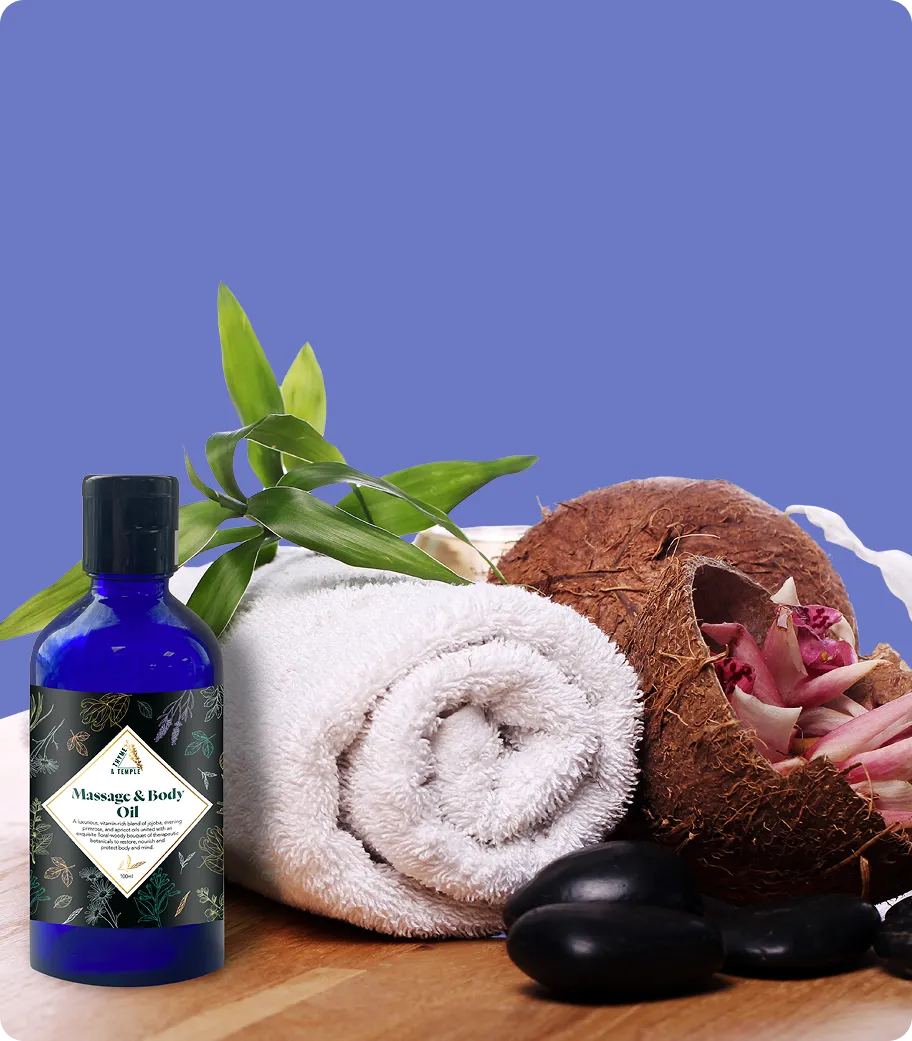 Massage and body oil bottle beside a rolled white towel, green leaves, coconut shell, and black stones.