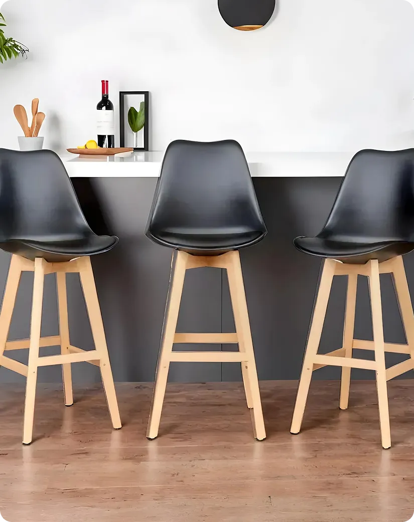 Three black bar stools with wooden legs in a modern kitchen with white counter and decor items.