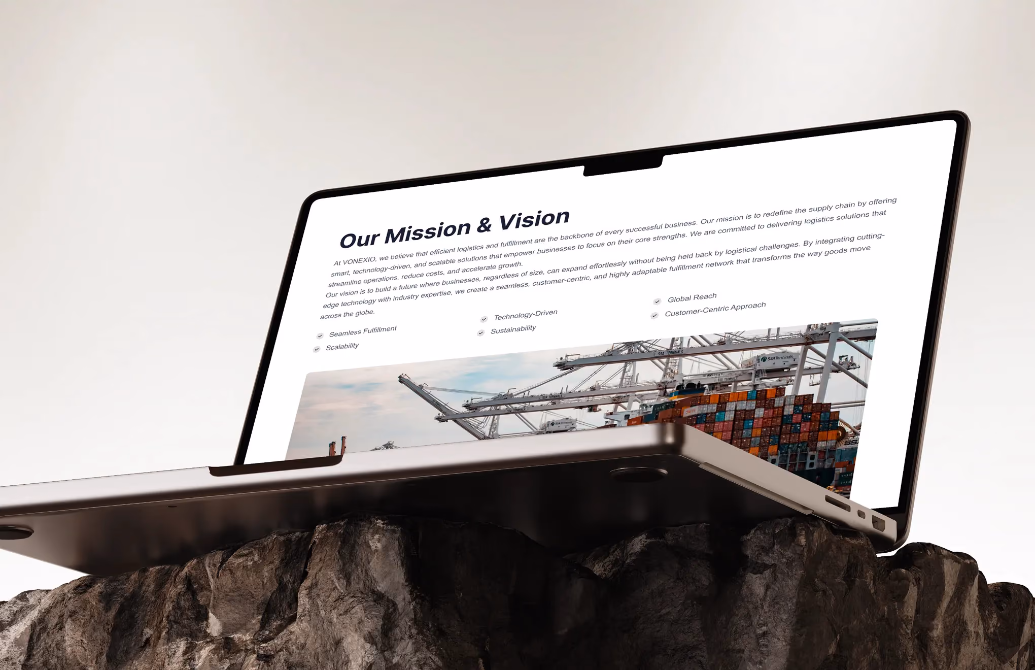 Laptop on rock showing a webpage with 'Our Mission & Vision' header and a shipping container image.