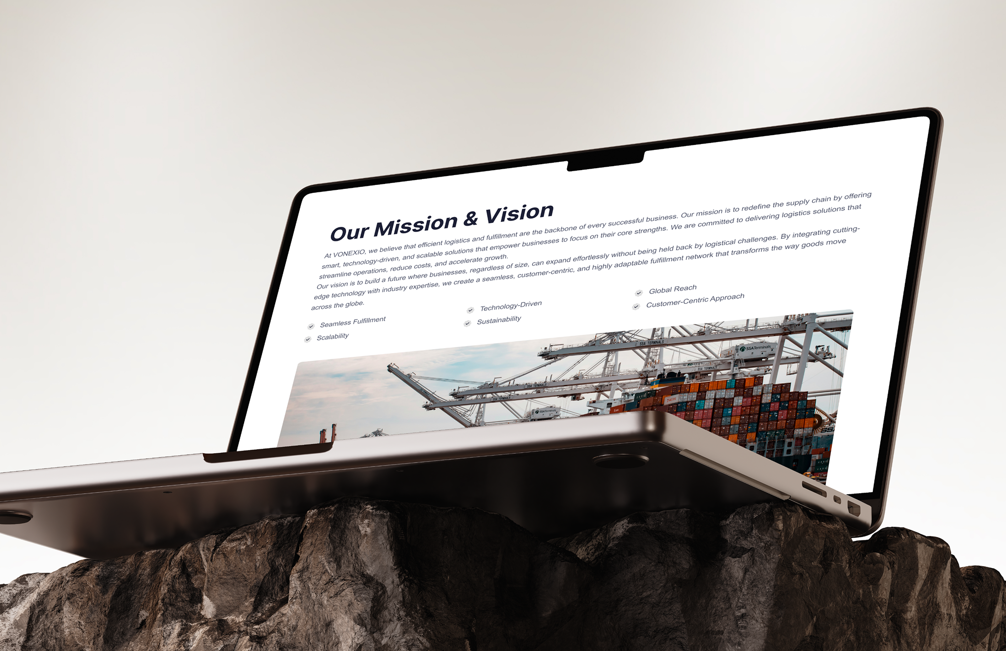 Laptop on rock showing a webpage with 'Our Mission & Vision' header and a shipping container image.