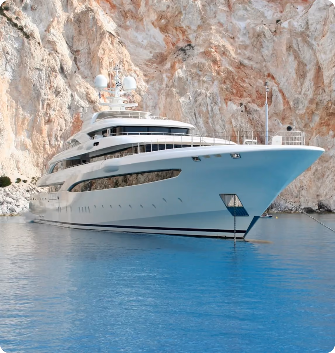 White luxury superyacht anchored in turquoise water beside dramatic red-rock coastal cliffs