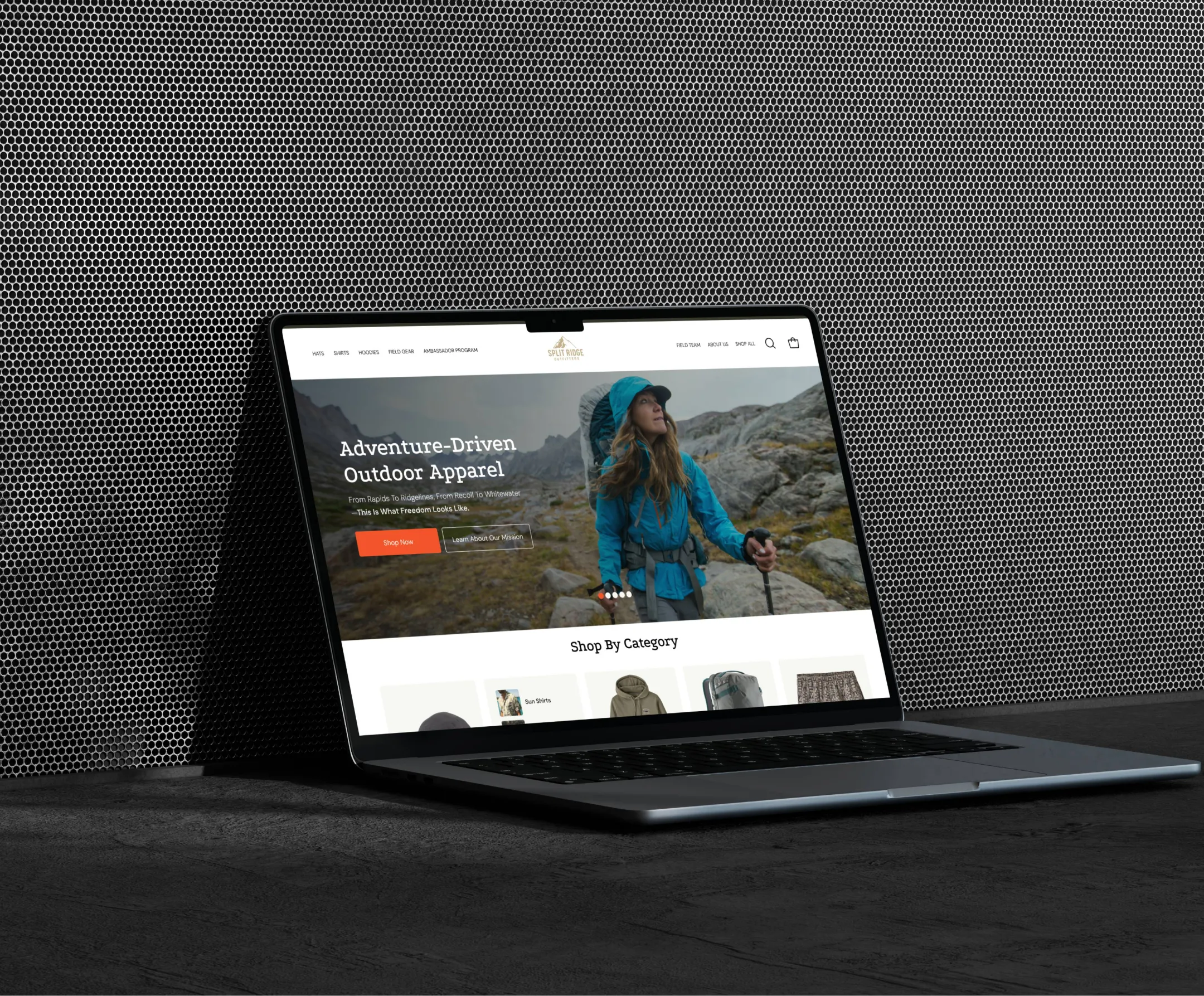 Laptop leaning on a perforated metal wall showing the Split Ridge Outfitters homepage hero with a hiker in the mountains