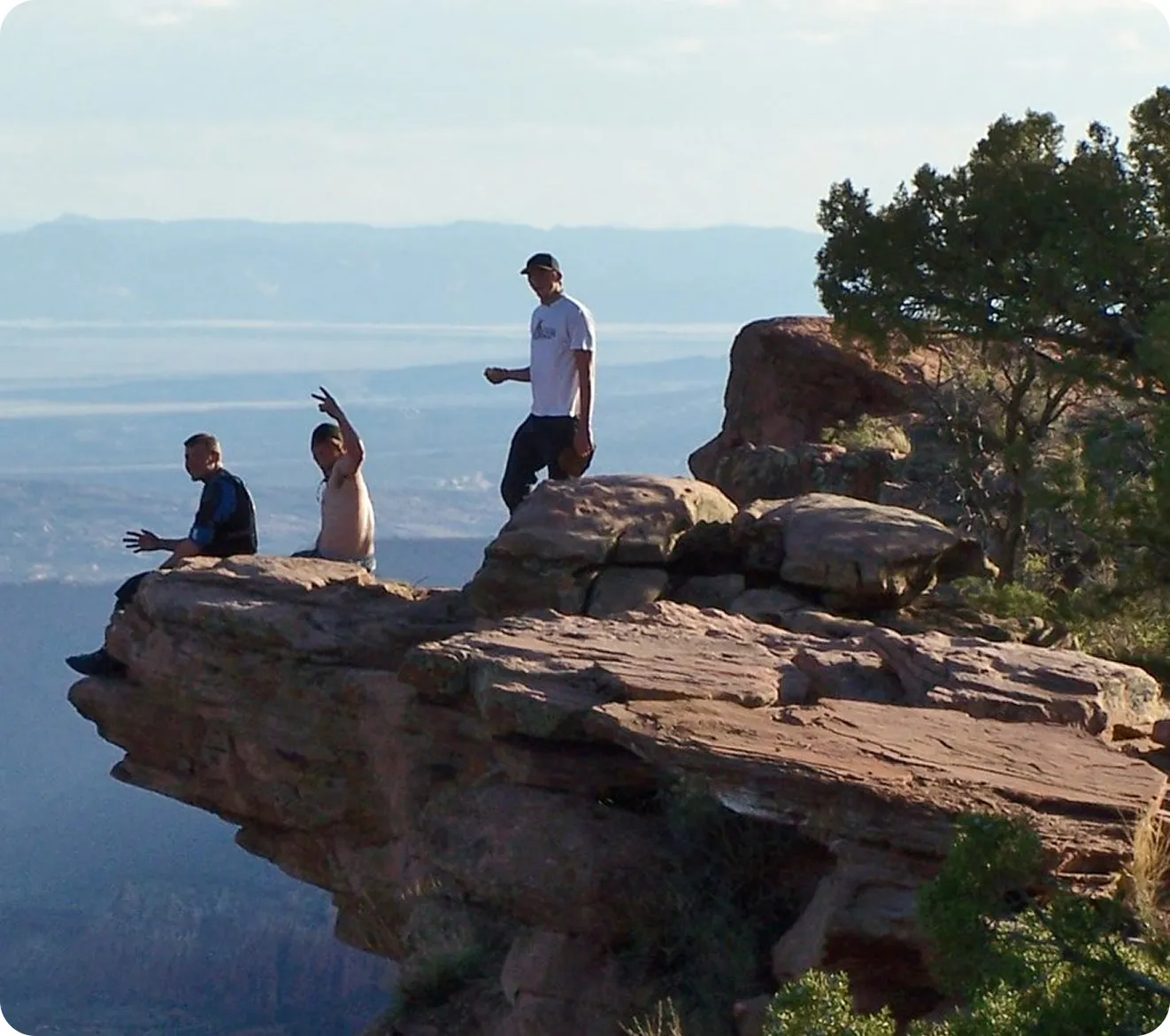 Three hikers on a sandstone cliff edge overlooking a wide canyon valley