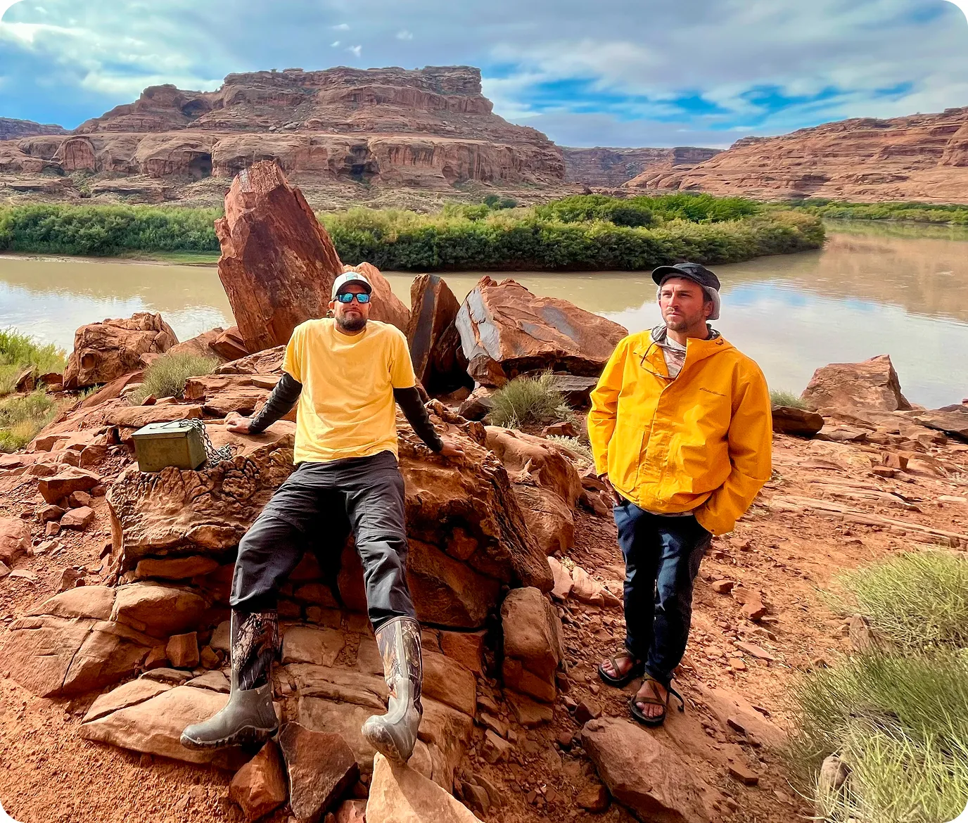 Two Split Ridge adventurers in yellow jackets on red rocks beside a desert canyon river