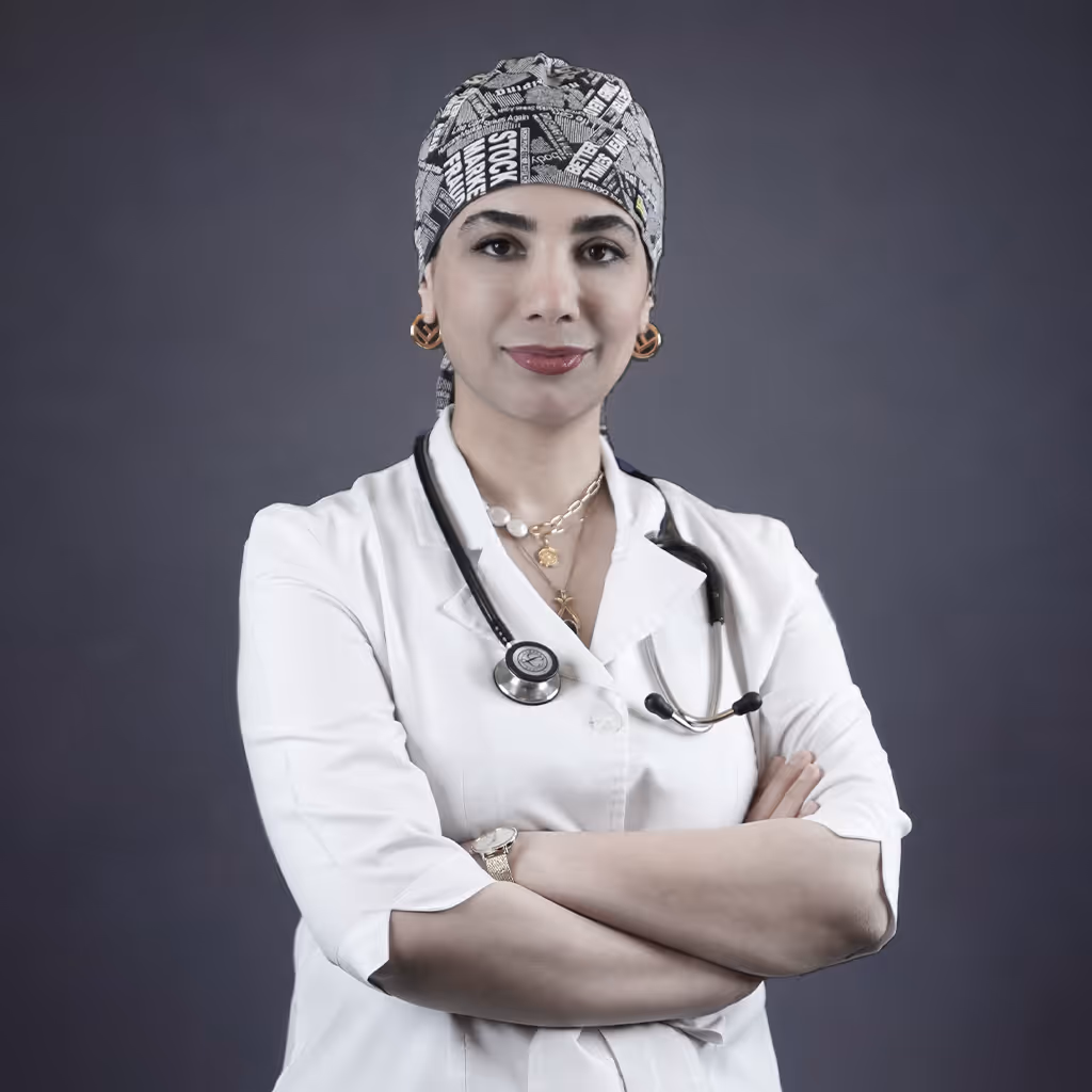 Female doctor wearing a white coat and patterned surgical cap with a stethoscope around her neck, standing with arms crossed.