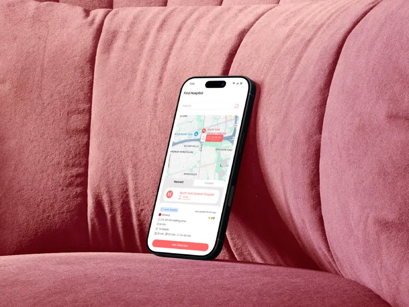 Smartphone resting on a pink velvet couch displaying a hospital finder app with a map and details for North York General Hospital.