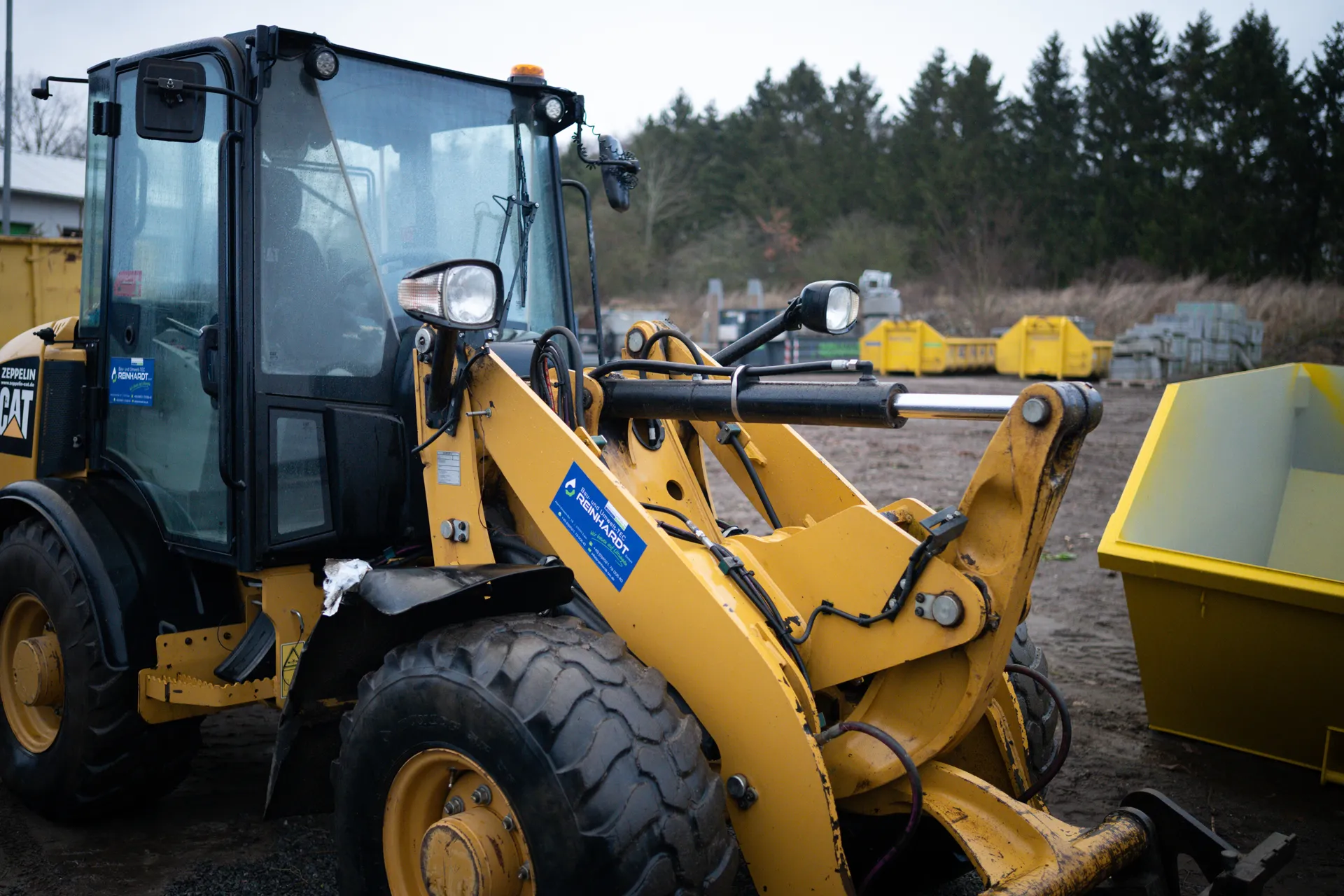 Gelber Caterpillar-Radlader steht auf einem Baugelände mit mehreren gelben Containern im Hintergrund.