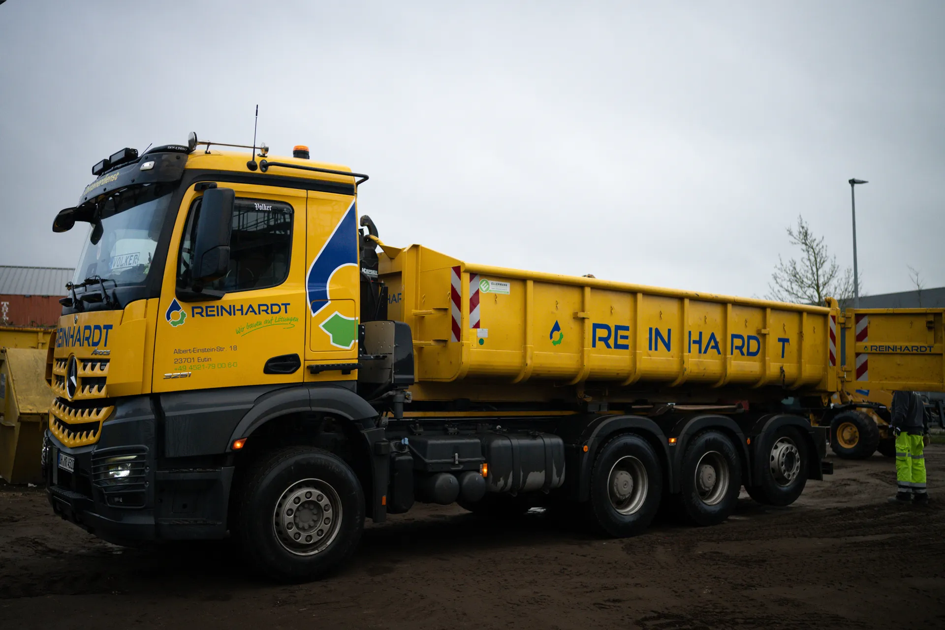 Gelber Muldenkipper mit dem Firmenlogo und der Aufschrift Reinhardt auf einer Baustelle.