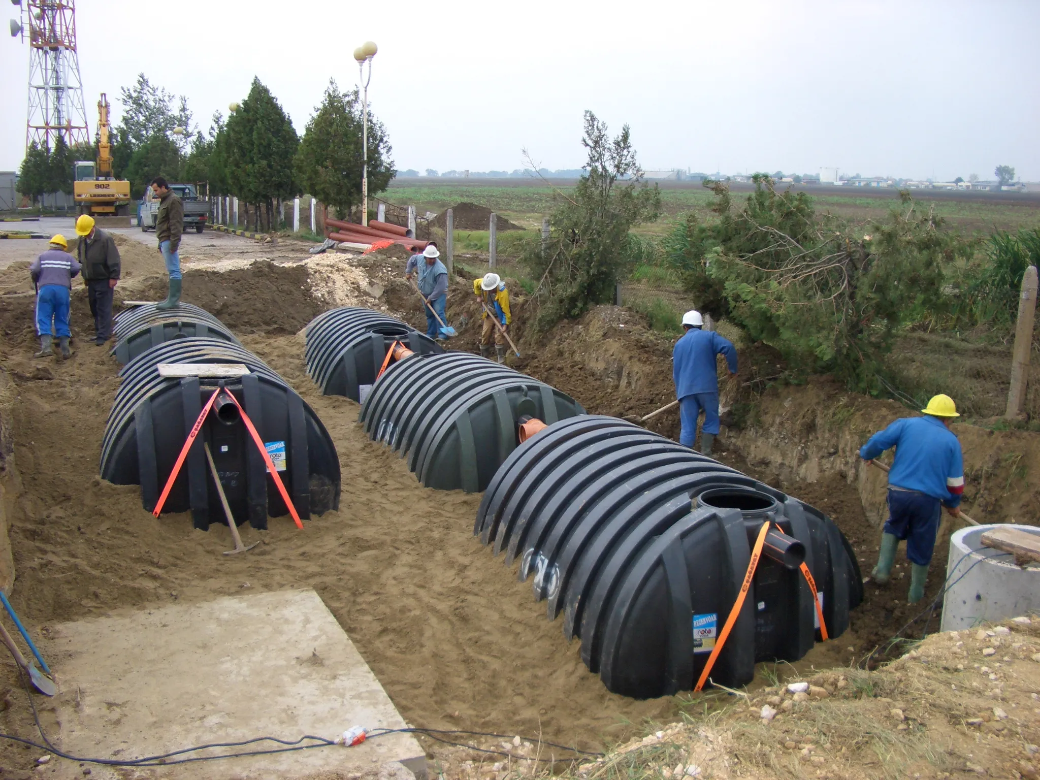 Zwei Bauarbeiter mit reflektierender Arbeitskleidung, die bei einer Straßenbaustelle auf einem Bürgersteig arbeiten.