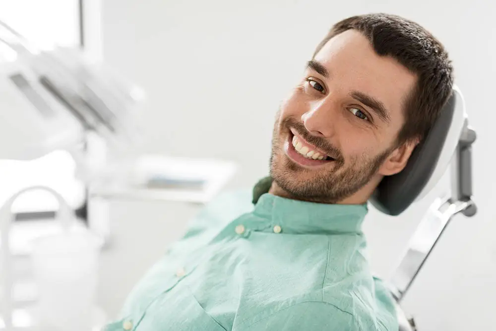 Smiling man with short dark hair and beard reclining on a dental chair.