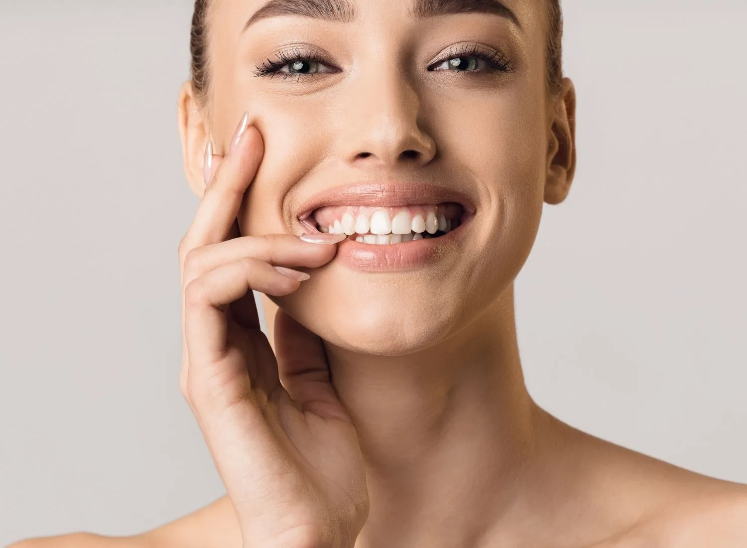 Close-up of a smiling woman gently holding her cheek, showing white teeth and clear skin.